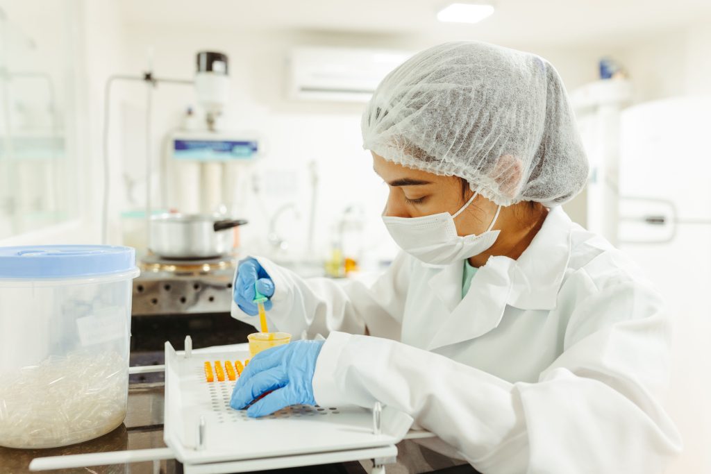 Laboratory worker in a hairnet, mask and gloves preparing capsules during dietary supplement production at Biveris